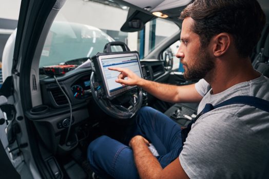 Male technician clicking on screen of diagnostic tool, attached to steering wheel of a car